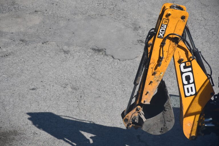 Braco Amarelo Da Maquina Escavadora E Sombra Do Lancamento Da Cubeta Na Terra aQ2Z5_5rhns